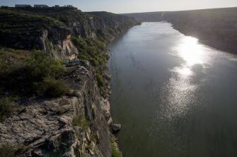 Aerial view of the Pecos River, highlighting the surrounding cliffs and vegetation under sunlight.