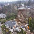Aerial view of a home that has been severely damaged by a landslide, showing debris and surrounding landscape. Aerial view of a home that has been severely damaged by a landslide, showing debris and surrounding landscape.
