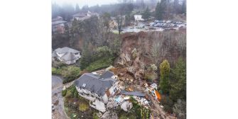 Aerial view of a home that has been severely damaged by a landslide, showing debris and surrounding landscape.