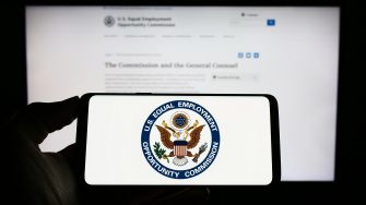 Logo of the U.S. Equal Employment Opportunity Commission displayed on a smartphone with a blurred website in the background.