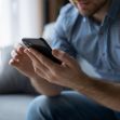A person holding a smartphone while sitting on a couch. A person holding a smartphone while sitting on a couch.