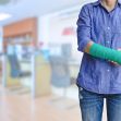 Person with a green cast on their arm, standing indoors in a workplace environment. Person with a green cast on their arm, standing indoors in a workplace environment.