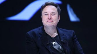 Elon Musk at a public event or conference, seated and speaking with a serious expression.
