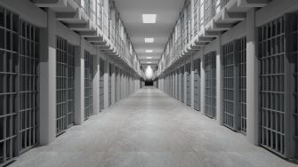 A long, empty prison hallway lined with barred cells on both sides.