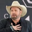 Garth Brooks speaking at a public event, wearing a cowboy hat and suit, with a serious expression. Garth Brooks speaking at a public event, wearing a cowboy hat and suit, with a serious expression.