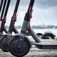 Electric scooters lined up in a row, set against a cloudy sky and waterfront background. Electric scooters lined up in a row, set against a cloudy sky and waterfront background.