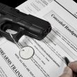 A handgun resting on top of a concealed handgun permit application form, with a pen and circular tag visible. A handgun resting on top of a concealed handgun permit application form, with a pen and circular tag visible.