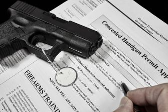 A handgun resting on top of a concealed handgun permit application form, with a pen and circular tag visible.