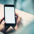 A person holding a smartphone with a blank screen on a table. A person holding a smartphone with a blank screen on a table.