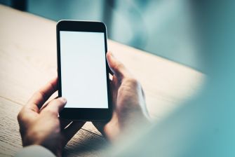 A person holding a smartphone with a blank screen on a table.
