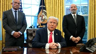 President Trump announces the new Gold Card during a press conference in the Oval Office, flanked by two officials.