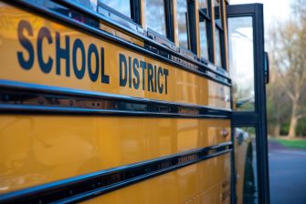Image of a yellow school bus with the words "SCHOOL DISTRICT" on its side, parked in a school environment.