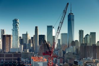 A view of a New York City skyline featuring construction cranes and skyscrapers.