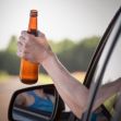 A person holding an open beer bottle out of a car window. A person holding an open beer bottle out of a car window.