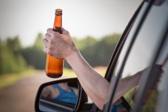 A person holding an open beer bottle out of a car window.