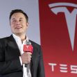 Elon Musk speaking at a Tesla event with the company logo in the background. Elon Musk speaking at a Tesla event with the company logo in the background.