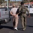 A law enforcement officer escorts an individual in handcuffs near a parked vehicle. A law enforcement officer escorts an individual in handcuffs near a parked vehicle.