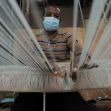 A man wearing a mask works at a weaving loom, highlighting the impact of trade policies on the textile industry in Ethiopia. A man wearing a mask works at a weaving loom, highlighting the impact of trade policies on the textile industry in Ethiopia.