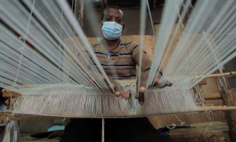A man wearing a mask works at a weaving loom, highlighting the impact of trade policies on the textile industry in Ethiopia.