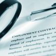 A magnifying glass and a clipboard positioned over an employment contract document, highlighting the text. A magnifying glass and a clipboard positioned over an employment contract document, highlighting the text.