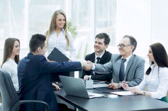 A group of professionals in business attire engaged in a meeting, with one man shaking hands with another across a conference table.