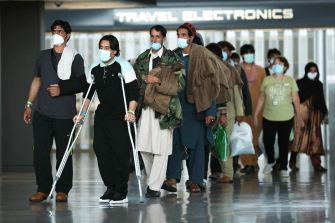 Group of Afghan evacuees arriving at an airport, wearing masks and being escorted through the terminal.