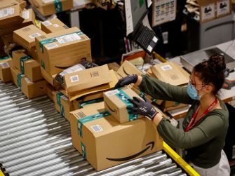 A warehouse worker organizes Amazon packages on a conveyor belt.