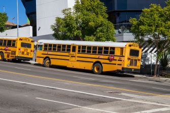 Yellow school buses parked along a street outside a school building.