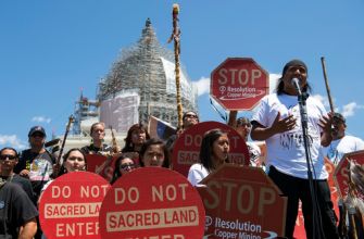 Protesters from the San Carlos Apache tribe holding signs opposing copper mining on sacred land at a demonstration.