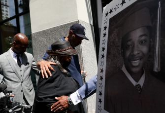 Family members of Jordan Neely at a press conference, one holding a sign with Neely's graduation photo.