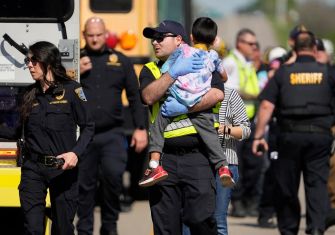 Emergency responders assist a child after a school bus crash involving a commercial truck, which resulted in fatalities and numerous injuries.