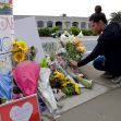 A woman kneels by a makeshift memorial adorned with flowers and signs, paying her respects. A woman kneels by a makeshift memorial adorned with flowers and signs, paying her respects.
