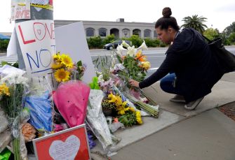 A woman kneels by a makeshift memorial adorned with flowers and signs, paying her respects.
