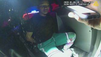 A man sitting in the back of a police car during a traffic stop.