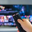 A hand holding a Netflix remote in front of a television displaying a Netflix interface. A hand holding a Netflix remote in front of a television displaying a Netflix interface.