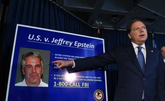 A man points at a poster detailing the case against Jeffrey Epstein, which includes his photo and a call to action for victims to contact the FBI.