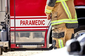 A firefighter standing next to a fire engine with "PARAMEDIC" labeled on the side.