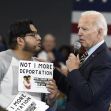 A scene depicting President Biden engaging with a protester holding a sign that reads "NOT 1 MORE DEPORTATION" during an event, amidst a gathering of supporters in the background. A scene depicting President Biden engaging with a protester holding a sign that reads "NOT 1 MORE DEPORTATION" during an event, amidst a gathering of supporters in the background.
