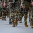 A group of military personnel in camouflage uniforms walking in formation, holding helmets. A group of military personnel in camouflage uniforms walking in formation, holding helmets.