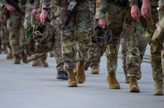 A group of military personnel in camouflage uniforms walking in formation, holding helmets.