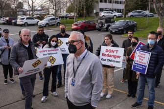 A group of protesters holding signs expressing concerns about the safety of children in relation to a new housing project for the homeless in front of a hotel in Kirkland, Washington.