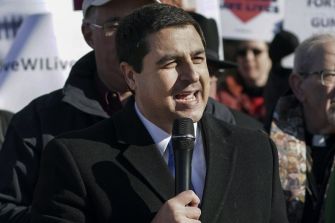 Wisconsin Attorney General Joshua Kaul speaking at a public event, holding a microphone and addressing a crowd.