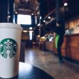 A Starbucks cup in the foreground with a blurred barista in the background at a Starbucks store. A Starbucks cup in the foreground with a blurred barista in the background at a Starbucks store.