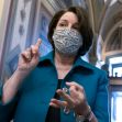 Senator Amy Klobuchar gestures while discussing antitrust legislation, wearing a mask in a legislative setting. Senator Amy Klobuchar gestures while discussing antitrust legislation, wearing a mask in a legislative setting.