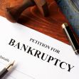 A close-up of a bankruptcy petition form with a gavel and a pen nearby. A close-up of a bankruptcy petition form with a gavel and a pen nearby.