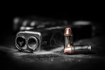 A close-up of a handgun with two bullets in the foreground, smoke gently rising from the gun.