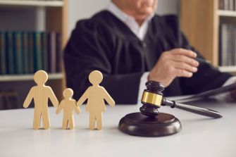 Wooden figures representing a family stand beside a judge's gavel on a table, emphasizing a child custody case in a courtroom setting.