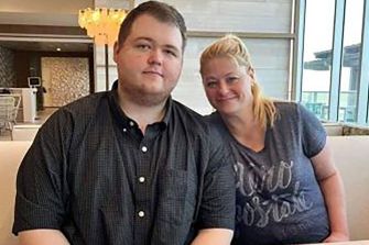 A man and a woman sitting together in a casual setting, with the woman smiling and the man looking directly at the camera.