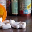 Close-up of spilled white prescription tablets from an orange pill bottle, with various labeled prescription bottles in the background. Close-up of spilled white prescription tablets from an orange pill bottle, with various labeled prescription bottles in the background.