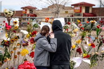 A couple paying their respects at a memorial adorned with flowers and notes following a mass shooting incident.